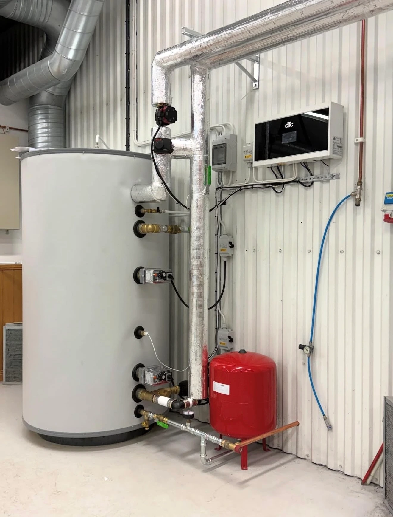 Varmvattenberedare och expansionskärl installerade mot vägg med rör och styrsystem.